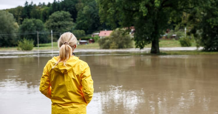 Γυναίκα με κίτρινο αδιάβροχο κοιτάζει ένα πλημμυρισμένο τοπίο