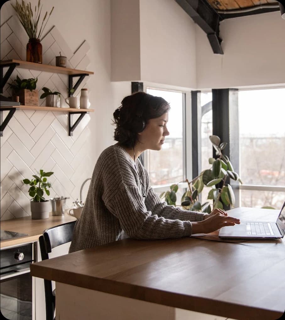 Γυναίκα που εργάζεται στο σπίτι της, στην κουζίνα και δουλεύει ανέμελη σε laptop