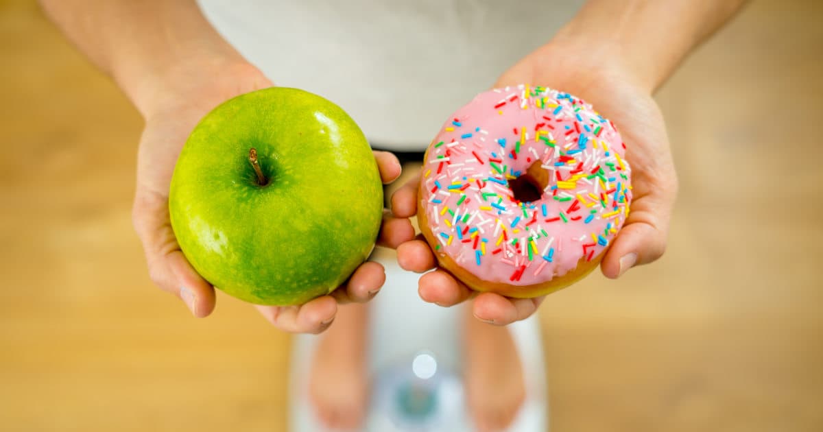 κοπελα κραταει ένα μήλο και ένα donut πάνω στη ζυγαριά